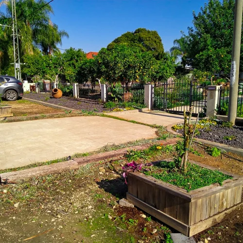 שטח חוץ עם ערוגות חדשות, עצי פרי ואזור מרוצף במהלך עבודות השדרוג.