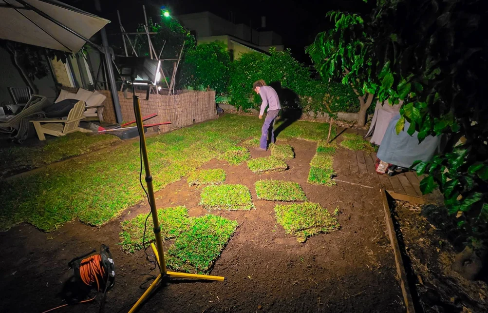 עבודות הנחת מרבדי דשא בחצר בשעות הלילה תחת תאורת פרוז'קטור.