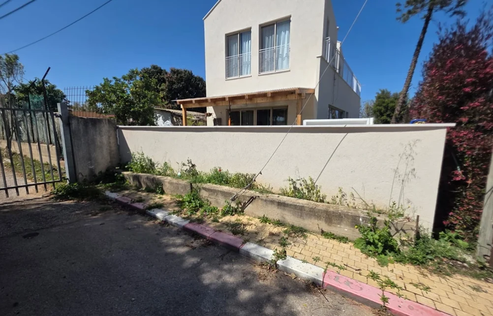 ערוגה צרה לאורך קיר החצר עם צמחייה דלילה ולא מסודרת לפני השדרוג.