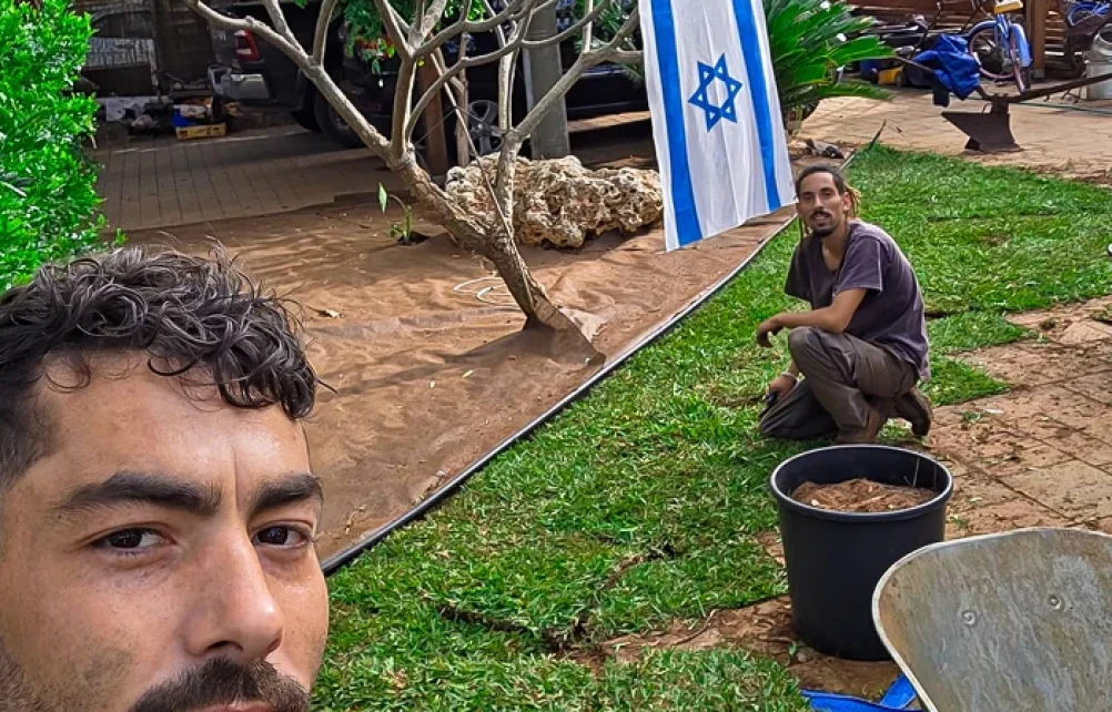 שני אנשי מקצוע במהלך עבודות בגינה, אחד עובד בהכנת הקרקע לצד המדשאה וכלי העבודה.