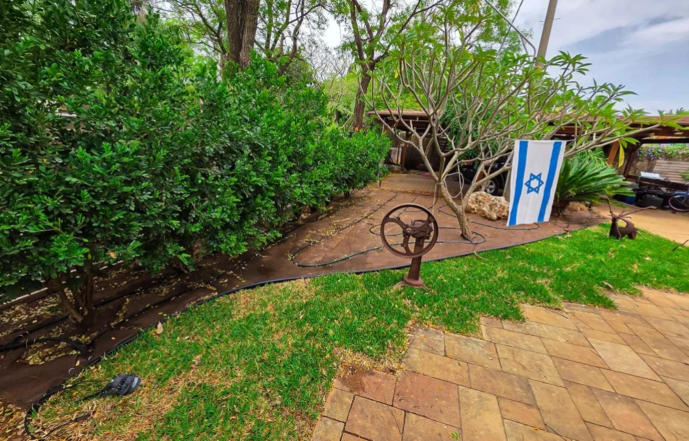 פינת גינה במהלך העבודה, עם צמחייה קיימת, אזור מרוצף וציוד גינון.