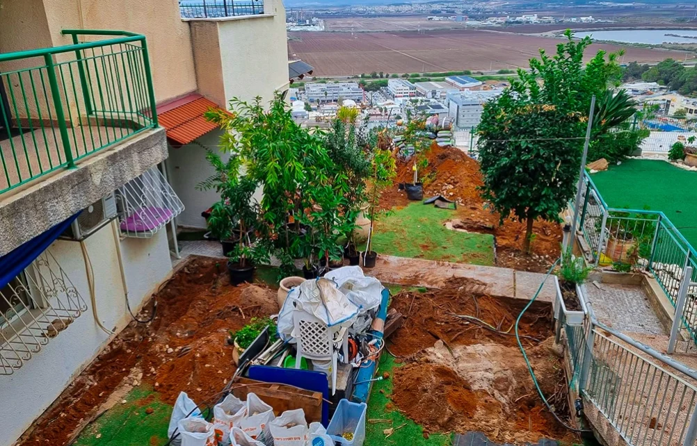 עבודות עפר והכנת תשתיות גינון בחצר מדורגת של בית פרטי, עם שקי חומרי בניין ומבט אל הנוף הפתוח.